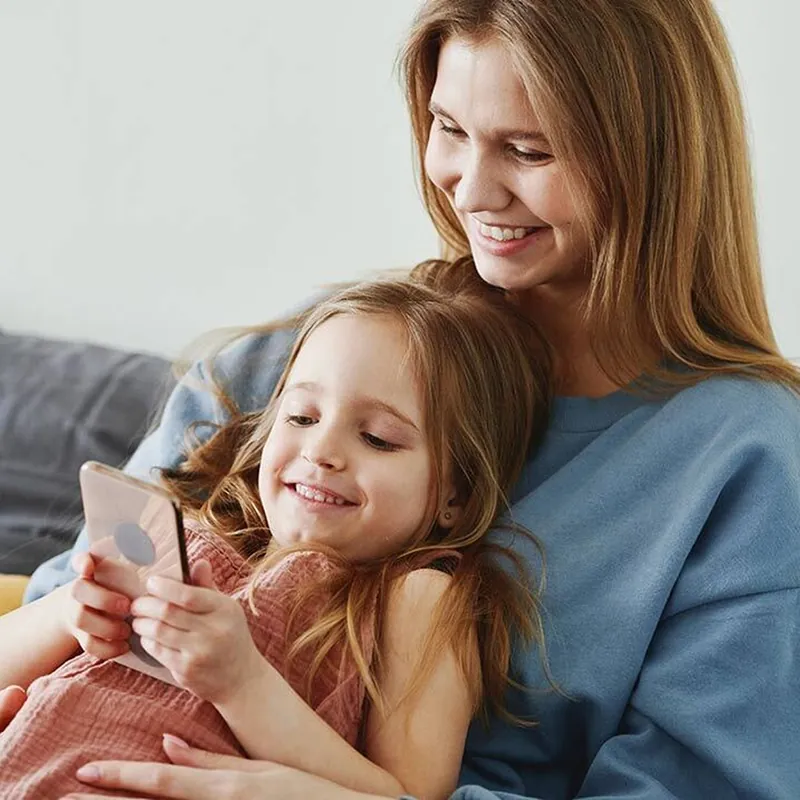 Mutter und Tochter sitzen auf dem Sofa und schauen gemeinsam auf ein Handy.
