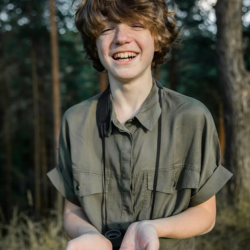 Lachender Teenager mit Fernglas im Wald.